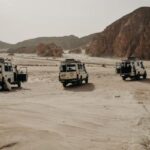 Autonomous Vehicles - Four jeeps are parked in the desert with mountains in the background