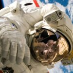 Space Technologies - This picture shows an american astronaut in his space and extravehicular activity suite working outside of a spacecraft. In the background parts of a space shuttle are visible. In the far background of the picture planet earth with it's blue color and white clouds is shown as well as a patch of black space.